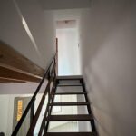 Escalera interior de estructura metálica y peldaños de madera hacia la planta alta.