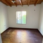 Ambiente de planta alta con piso de madera, techo de madera y ventana con rejas.